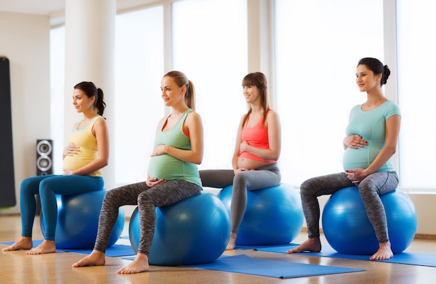 pregnancy, sport, fitness, people and healthy lifestyle concept - group of happy pregnant women exercising on ball in gym