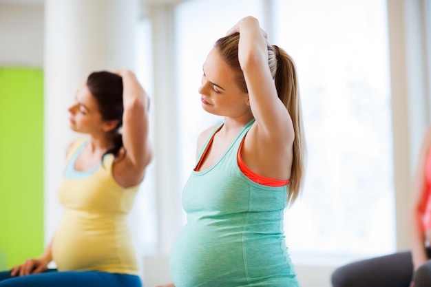 妊娠、スポーツ、フィットネス、人々、健康的なライフ スタイル コンセプト - ジムで運動する幸せな妊娠中の女性のグループ