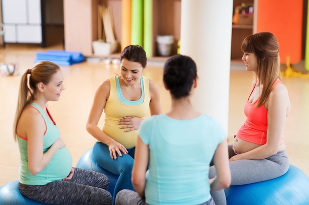 Foto gravidanza, sport, fitness, persone e concetto di stile di vita sano - gruppo di donne incinte felici che si siedono e parlano sulle palle in palestra