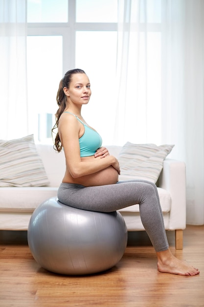 pregnancy, sport, fitness, people and healthy lifestyle concept - happy pregnant woman exercising on fitball at home