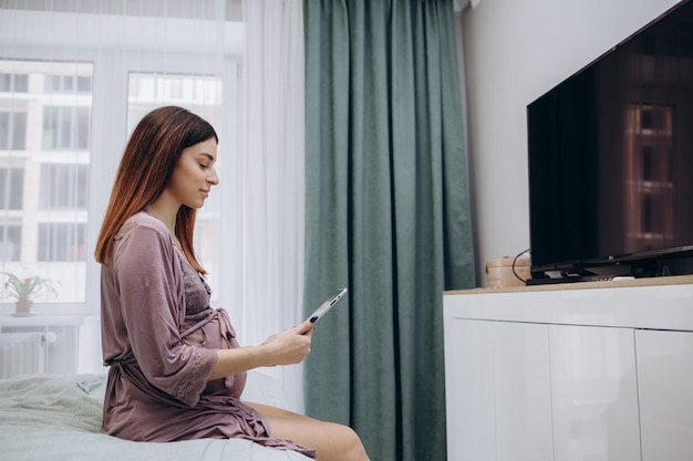 Pregnancy technology people and expectation concept close up of pregnant woman with tablet pc computer in bed at home