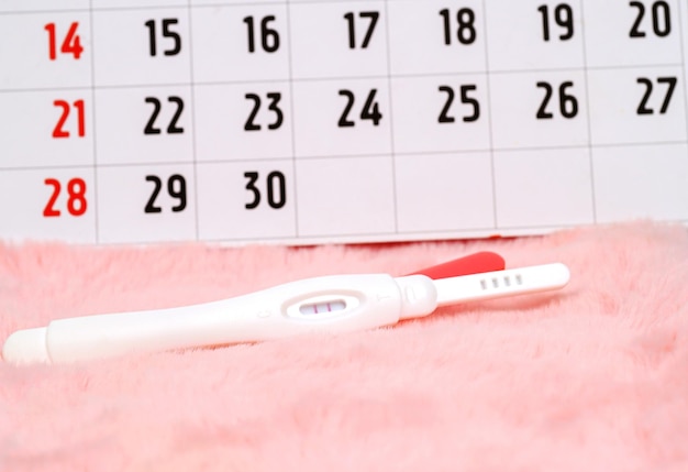 Foto dispositivo per test di gravidanza per determinare una donna incinta sul calendario concetto di salute e medicina