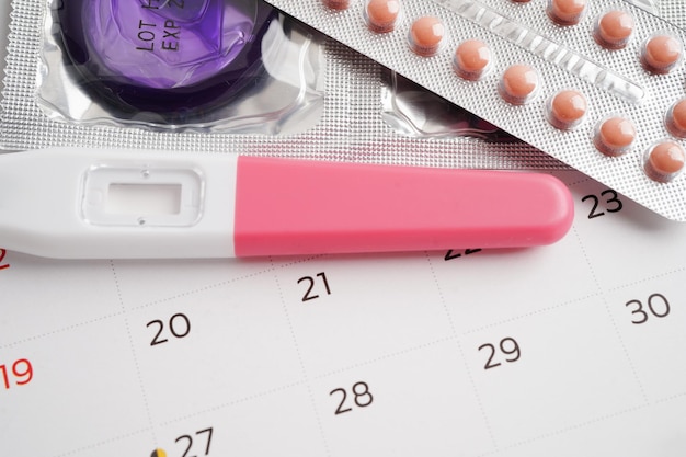 Photo pregnancy test with birth control pills and condom for female on calendar ovulation day