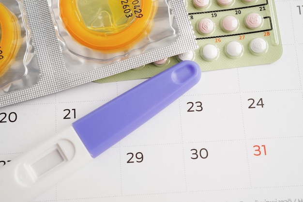 Photo pregnancy test with birth control pills and condom for female on calendar ovulation day