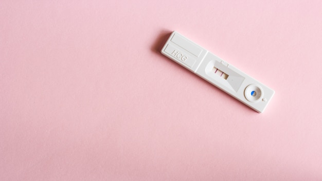 Pregnancy test with pregnant result on pink background.