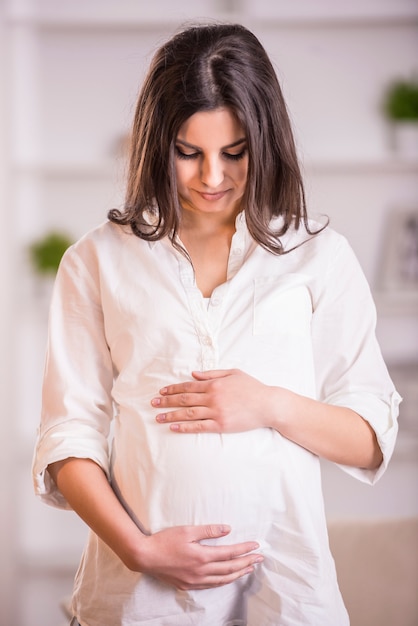 Pregnant adult woman looking on her belly at home.