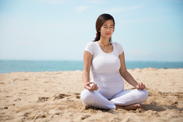 Donna asiatica incinta che fa yoga nella riva di mare