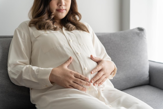 妊娠中のアジア人女性は腹に手を握り赤ちゃんに触れ自分の健康を心配しています美しい幸せな妊娠中の女性妊娠中の優しい気分の写真
