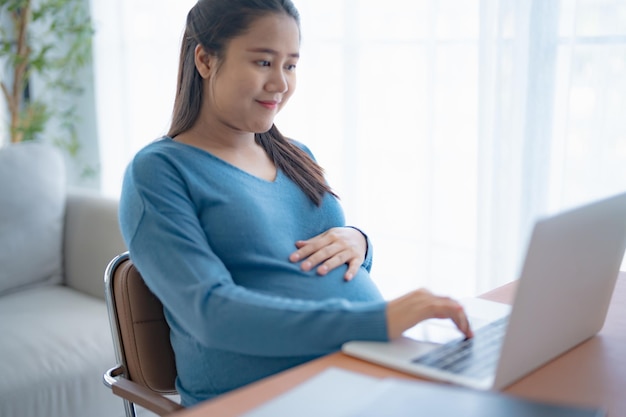pregnant asian woman using laptop at home pregnant businesswoman typing on laptop working on remote project in home office pregnancy concept