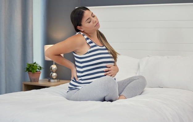 Foto letto incinta e donna con mal di schiena problemi di maternità e ansia con dolori muscolari e crampi gravidanza donna o donna in camera da letto contrazioni e ansia per problemi di salute o stress