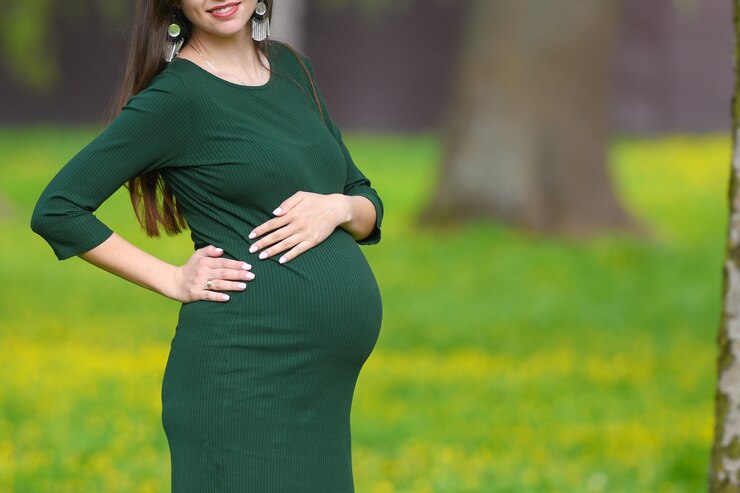 Pregnant belly closeup. Closeup on the belly of a pregnant woman wearing a long green dress, a new concept of life, a place for writing. Copyspace.