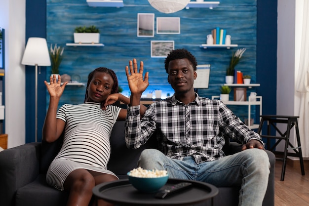 Pregnant black couple waving at video call camera