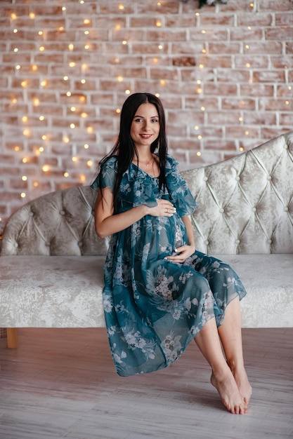 Pregnant bride brunet is preparing to become a mother and wife Long turquoise dress on a girl's body Curly hair and a beautiful smile on the woman's face Two months before birth