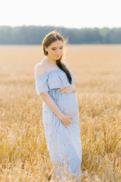 Pregnant brown-haired woman on maternity leave in a high Barley-wheat field