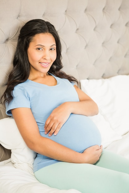 Pregnant brunette on bed at home