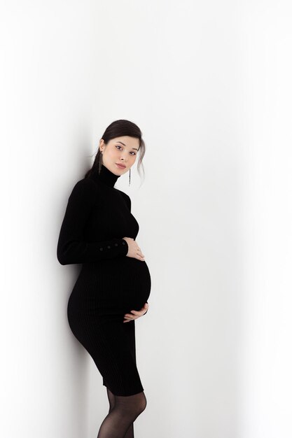 Pregnant brunette in a black dress with a neck on a white background