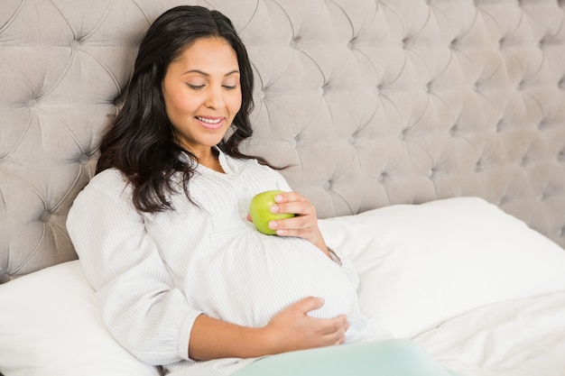 Pregnant brunette holding apple in bedroom