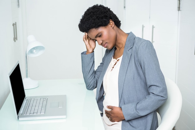 Pregnant businesswoman touching her head and belly in the office