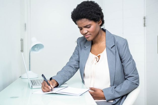 Scrittura incinta della donna di affari sul taccuino in ufficio