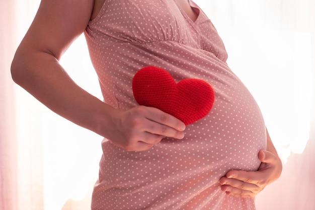Беременная кавказка с символом красного сердца, держащая живот