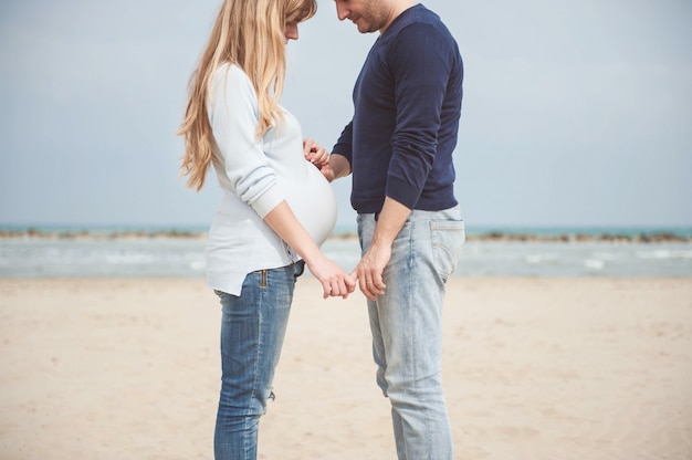 写真 ビーチで妊娠中のカップル。腹に手を。