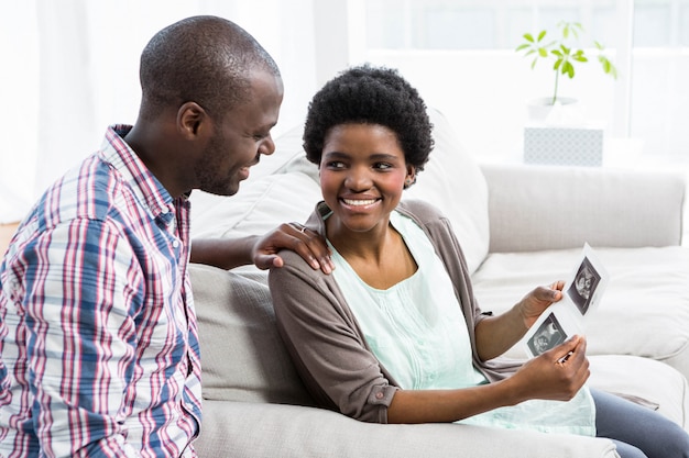 Pregnant couple sitting on sofa and looking at ultrasound scan at home