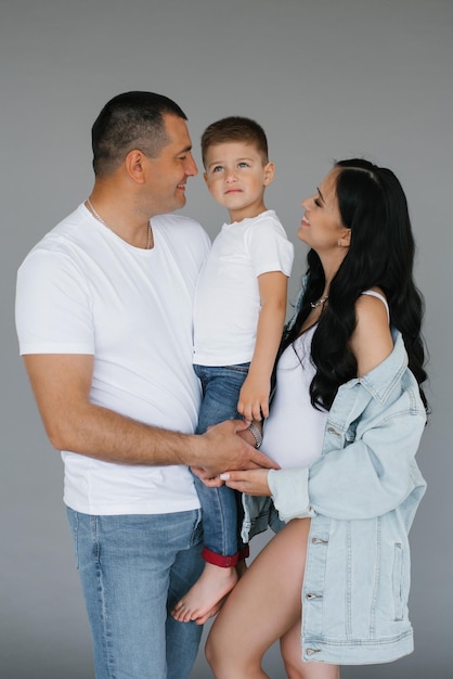 Pregnant couple a young family with a young son stand on a gray background laughing and waiting