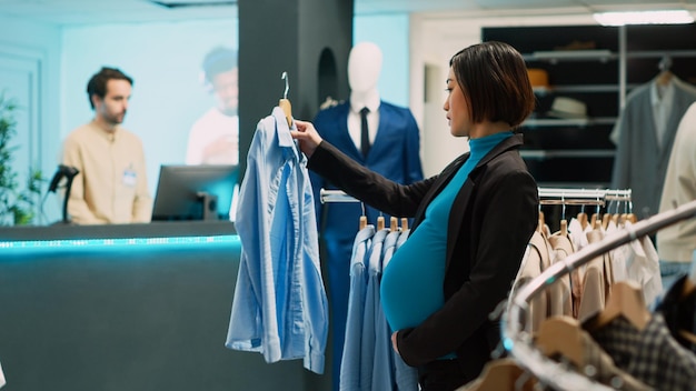 Pregnant customer analyzing trendy clothes on hangers