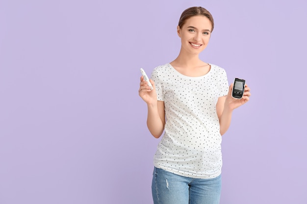 Pregnant diabetic woman with digital glucometer and lancet pen on color surface