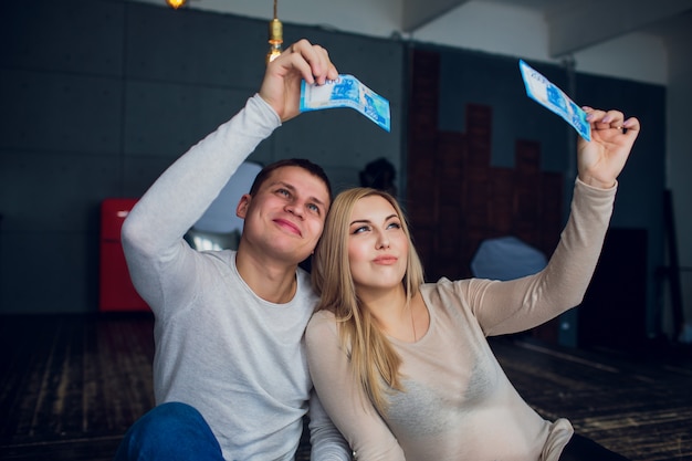 La famiglia incinta con i soldi e i vestiti del bambino si siedono su un divano della casa. bilancio familiare.