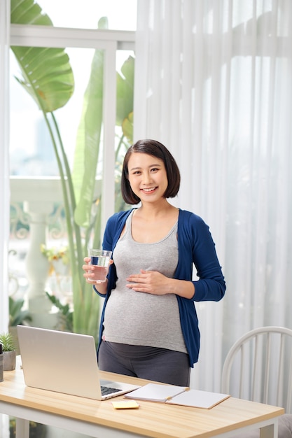 Pregnant freelancer using laptop near glass of water