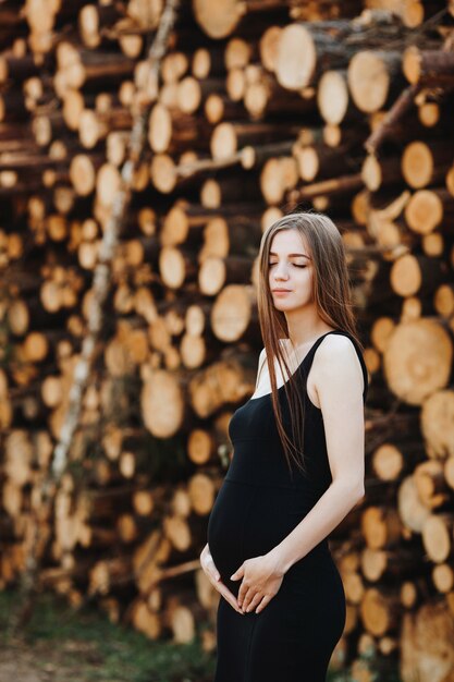 Беременная девушка в черном платье стоит на размытом фоне природы
