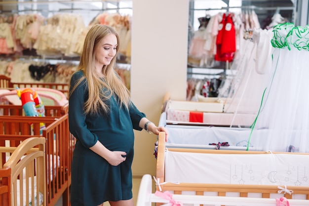 임신 한 여자는 가게에서 아기 침대를 선택합니다.