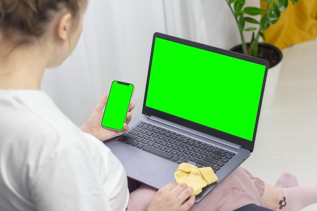 A pregnant girl on the couch with a phone in her hands a laptop on her lap a green screen