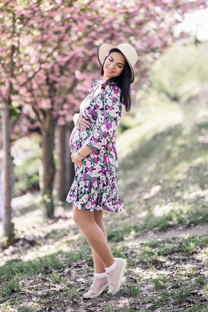 A pregnant girl in a dress near the sakura in the garden