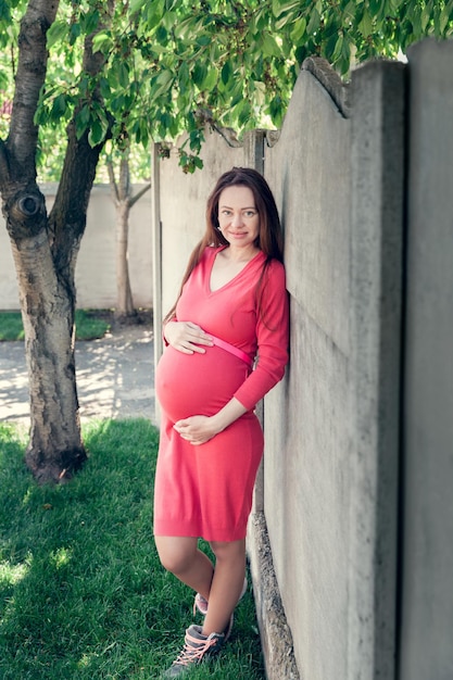 Pregnant girl dressed in pink dress, holds herself tummy