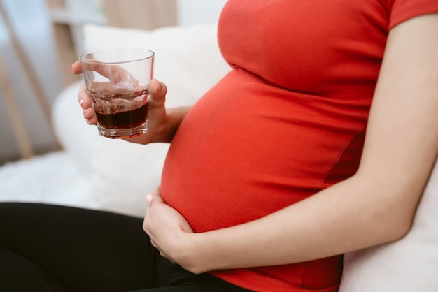 La ragazza incinta beve alcolici. lei tiene un bicchiere di alcol.