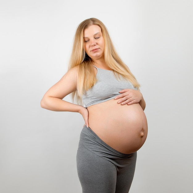 A pregnant girl on a gray background Big stomach back pain