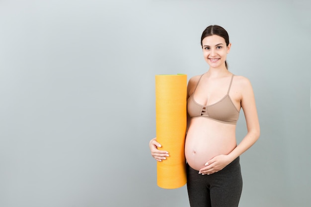 Ragazza incinta con tappetino da yoga in piedi su sfondo colorato studio girato spazio libero per il design