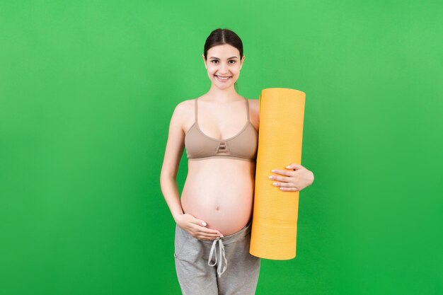 Photo pregnant girl holding yoga mat standing over colored background studio shot free space for design