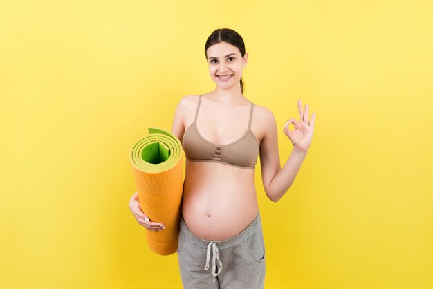 Foto ragazza incinta con un tappetino da yoga in piedi su uno sfondo colorato