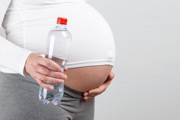 A pregnant girl holds a bottle of water the importance of a large amount of fluid for the expectant mother