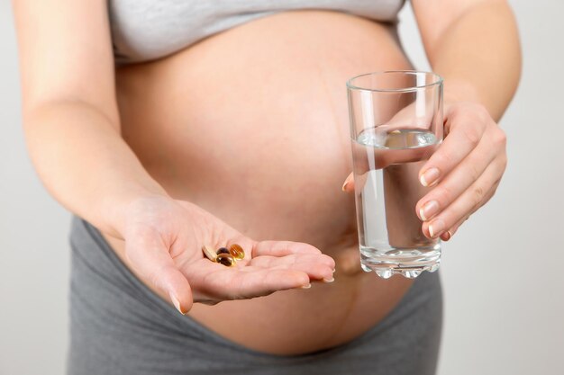 임신한 소녀는 약과 물 한 잔을 들고 있다 엄마와 아이를 위한 비타민의 이점