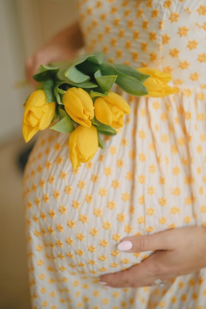 A pregnant girl holds yellow tulips near the abdomen