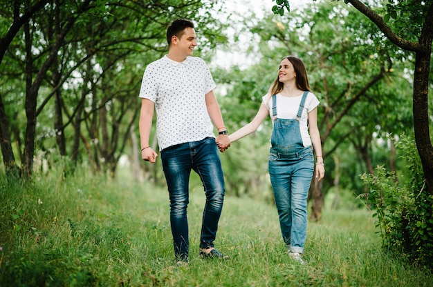 Pregnant girl and husband goes in the outdoor in the garden with trees.