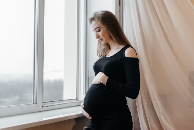 A pregnant girl is breathing fresh air from the window.