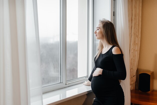 A pregnant girl is breathing fresh air from the window.