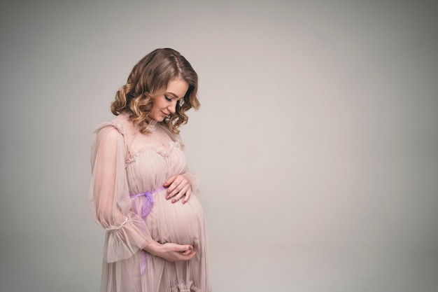 A pregnant girl is holding her belly. A young mother is expecting the birth of a child. Woman gently hugs her baby in the belly.