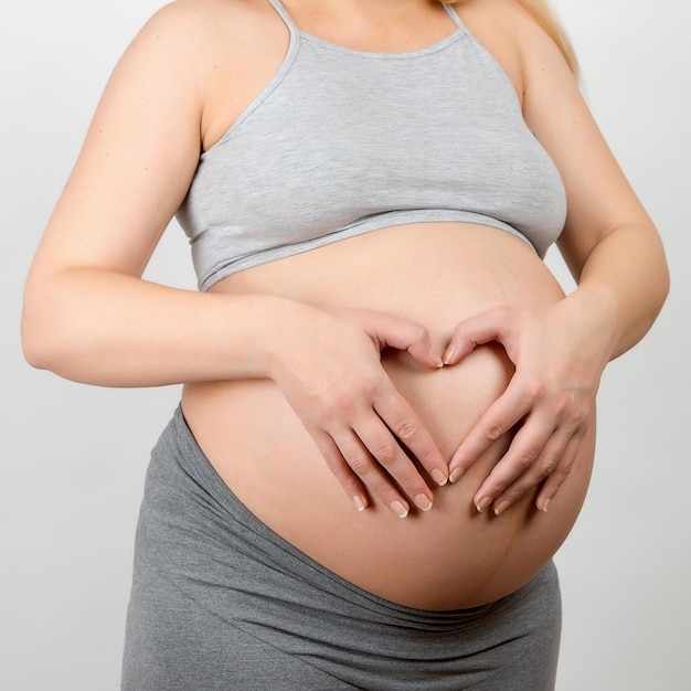 A pregnant girl keeps her hands on her stomach in the shape of a heart