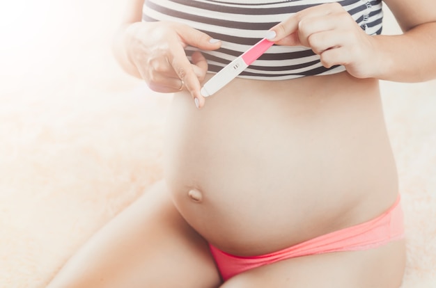 A pregnant girl on a large term with a pregnancy test, in hands, on the background of the tummy